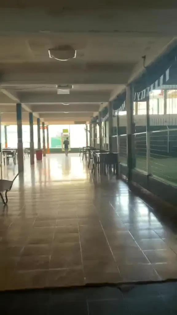 Pasillo cubierto con piso cerámico y ventanales hacia la cancha