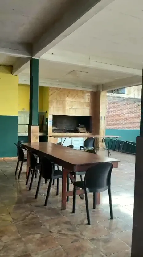 Mesas largas de madera con sillas negras frente a la parrilla de ladrillo